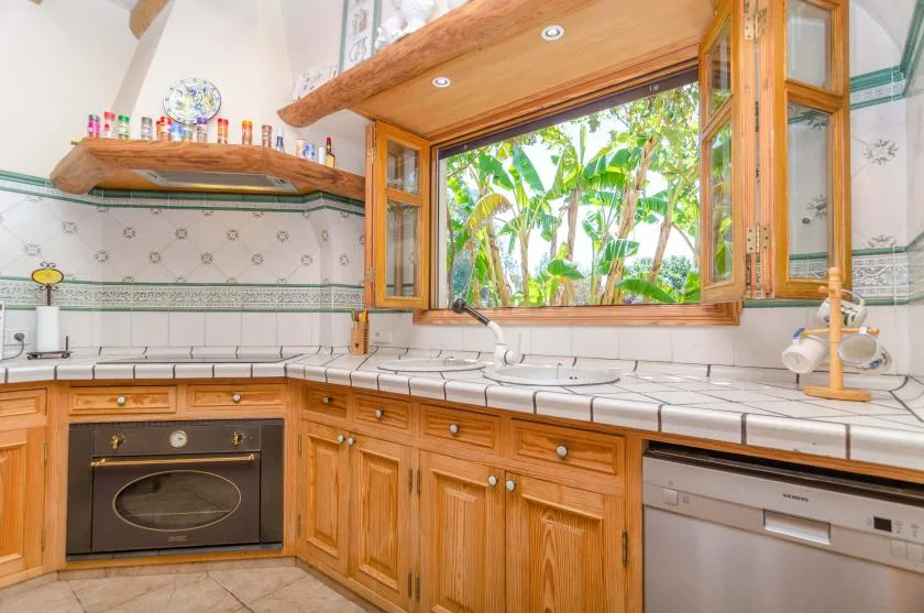 A bright kitchen with wooden cabinetry and an open window overlooking greenery.