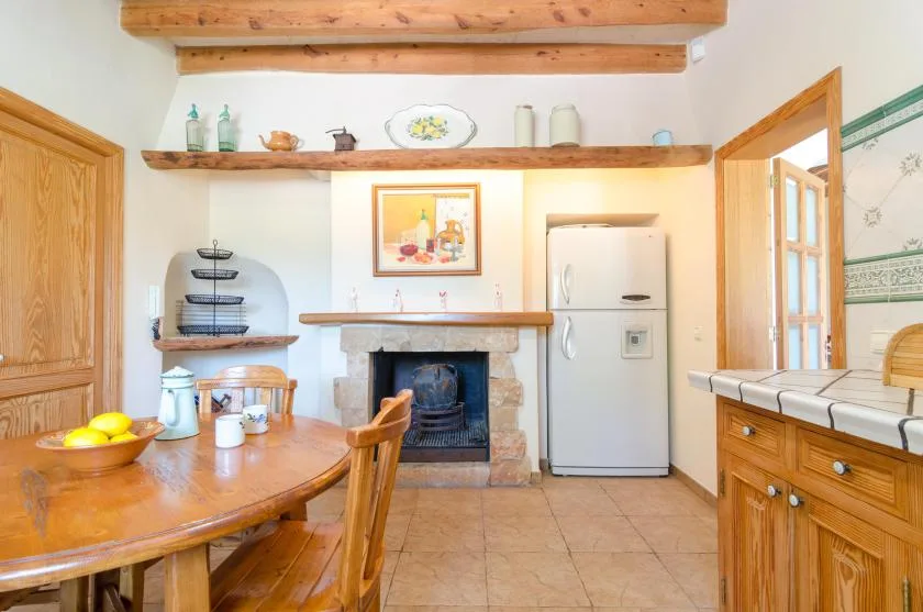 A rustic kitchen and dining area with a wooden table, fireplace, and refrigerator.