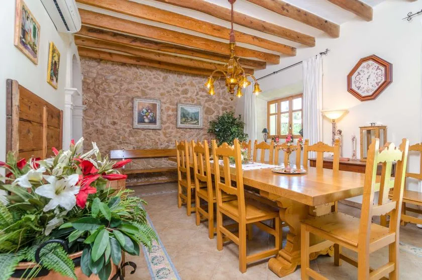 A dining room with a long wooden table and chairs beneath exposed ceiling beams.