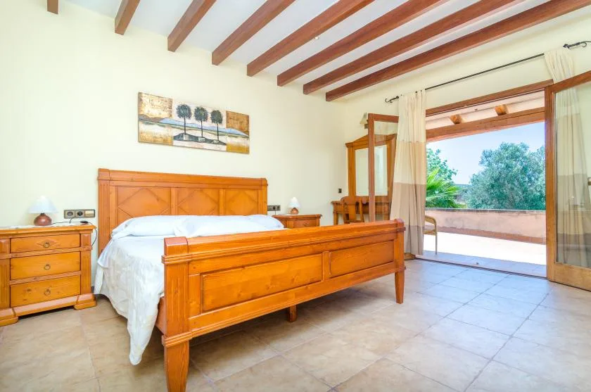 A bedroom with a wooden bed and an open glass door to the terrace.