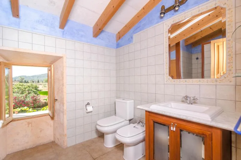 A tiled bathroom with a toilet, bidet, and vanity beside a window.