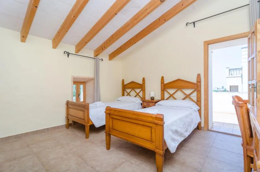 A bright bedroom with two wooden beds beneath exposed ceiling beams.