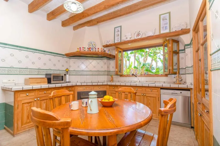 A kitchen with wooden cabinets, a central table, and a window overlooking greenery.