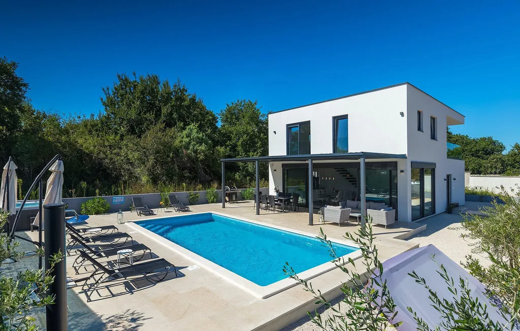 Una casa moderna da a una piscina con asientos de descanso en el patio.