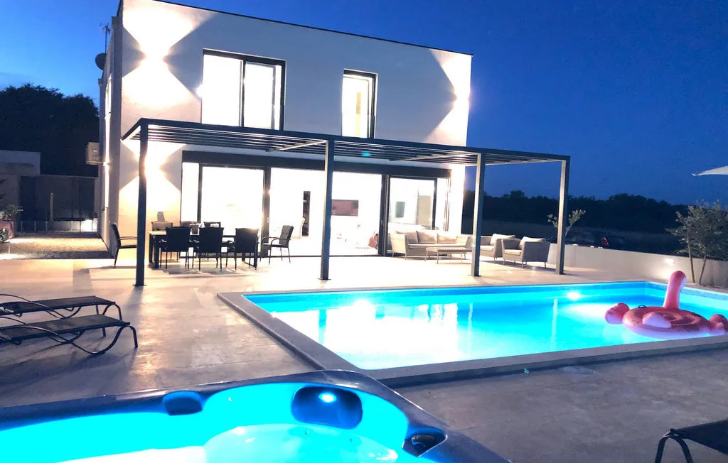 Piscina exterior y jacuzzi junto a una casa moderna al anochecer.