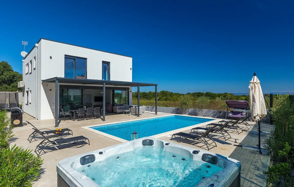 Una casa blanca moderna da a una piscina y una bañera de hidromasaje en un patio soleado.