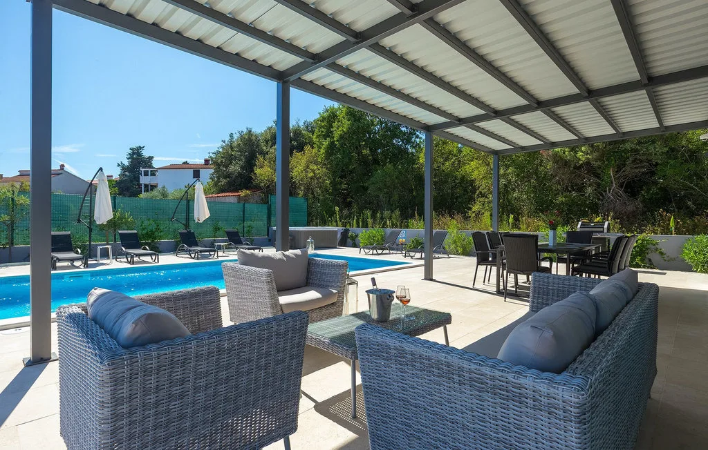 Un patio exterior cubierto con asientos junto a una piscina y una mesa de comedor.