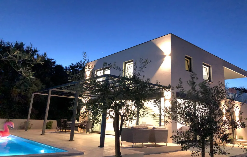 Una casa moderna al anochecer, con patio iluminado y piscina.