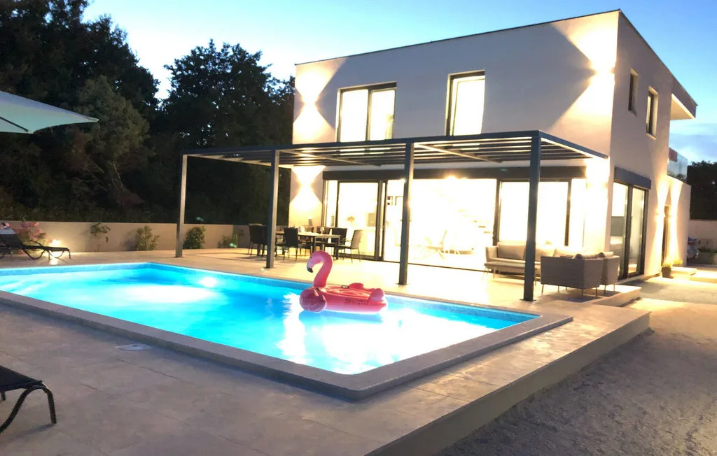 Una casa moderna se encuentra junto a una piscina iluminada al anochecer.
