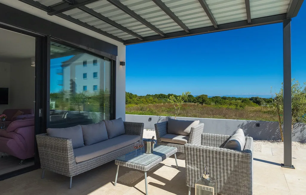 Una zona exterior cubierta con asientos de mimbre y vistas a la vegetación.