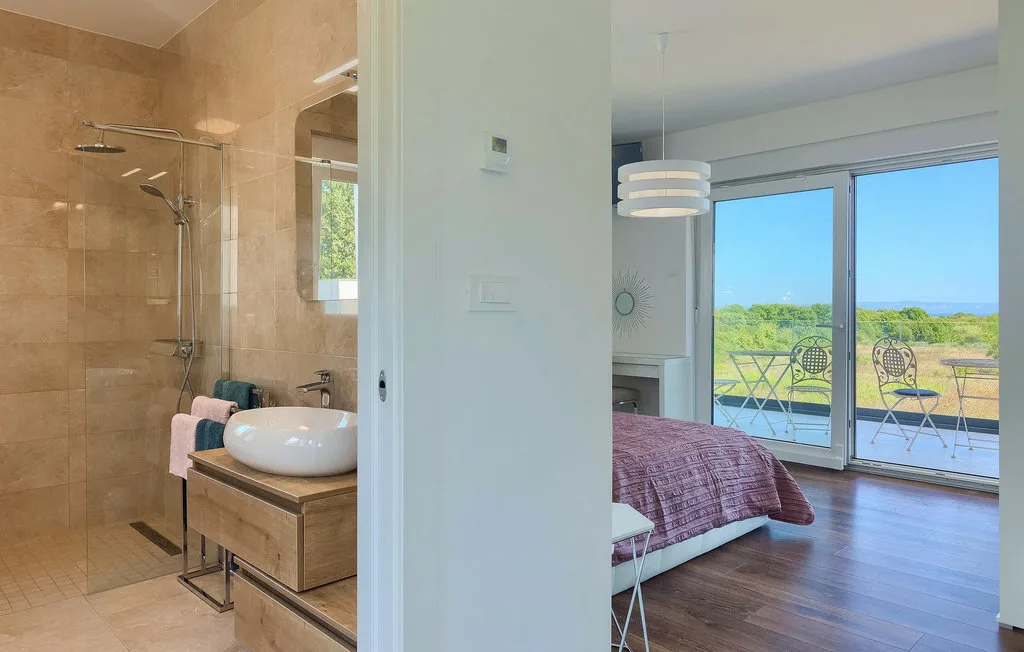 Un dormitorio con una cama junto a un baño y grandes ventanales con vista al balcón.