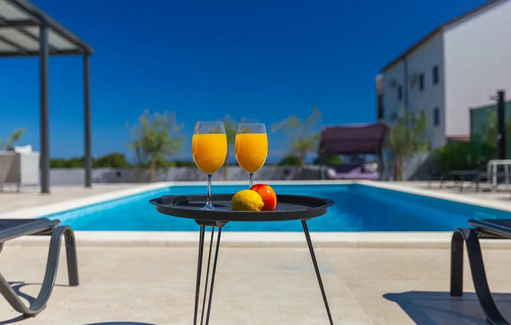 Una piscina con una mesa pequeña que sostiene dos bebidas y fruta.