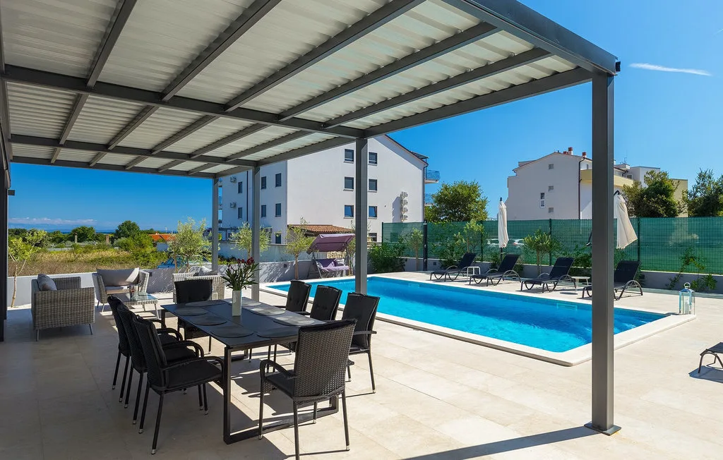 Una zona de comedor exterior cubierta da a una piscina y tumbonas.