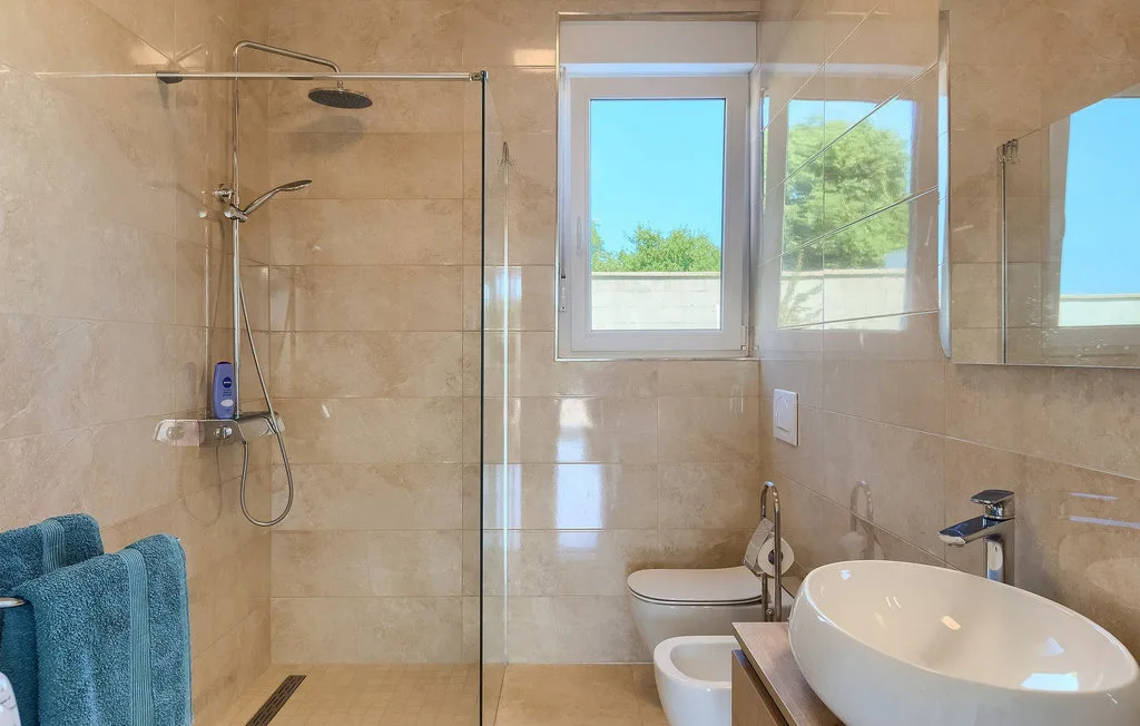 Un baño alicatado con una ducha de cristal y una ventana sobre el inodoro.