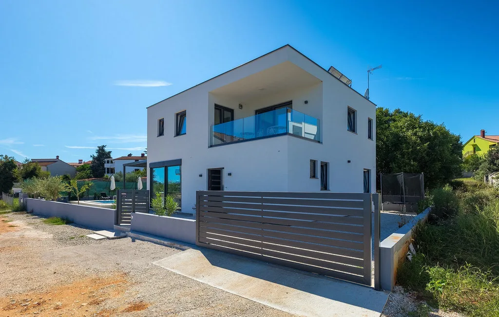 Una casa moderna de dos plantas con balcón está detrás de una puerta metálica.