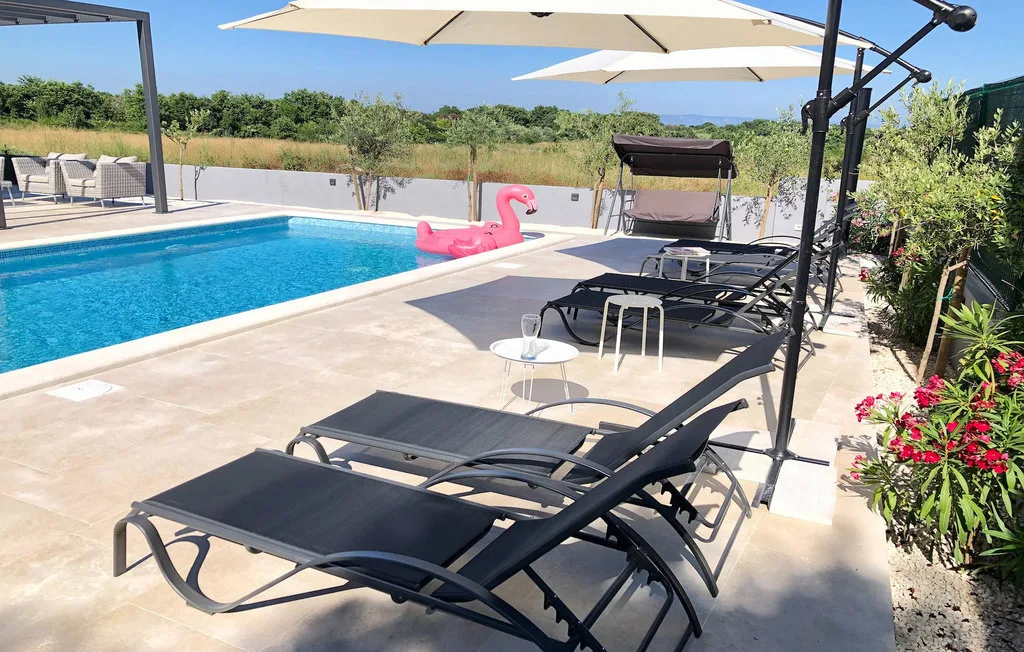 Un patio junto a una piscina tiene tumbonas y grandes sombrillas.