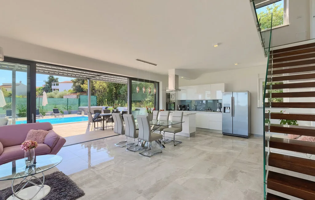 Sala y comedor de concepto abierto con cocina y puertas de vidrio hacia una piscina.