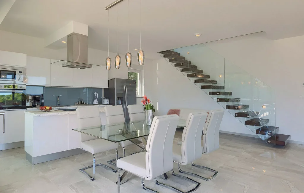 Una cocina y comedor modernos con una mesa de vidrio y una escalera abierta.