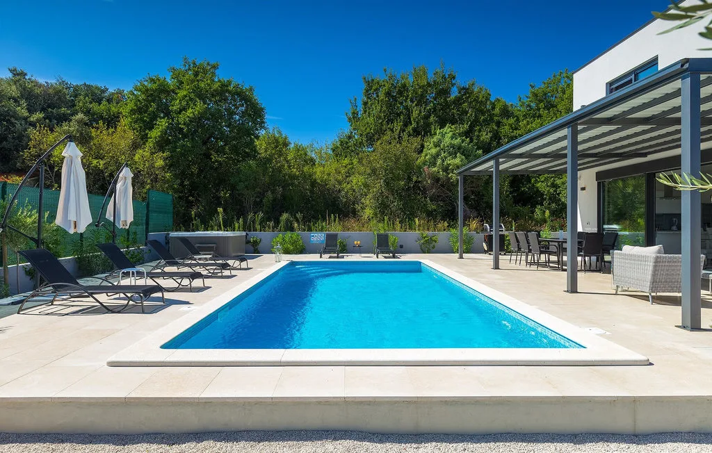 Una piscina al aire libre junto a un edificio moderno, con tumbonas alrededor.