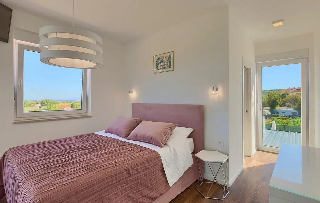 Un dormitorio con una cama, ropa de cama malva y ventanas con vistas a zonas verdes.