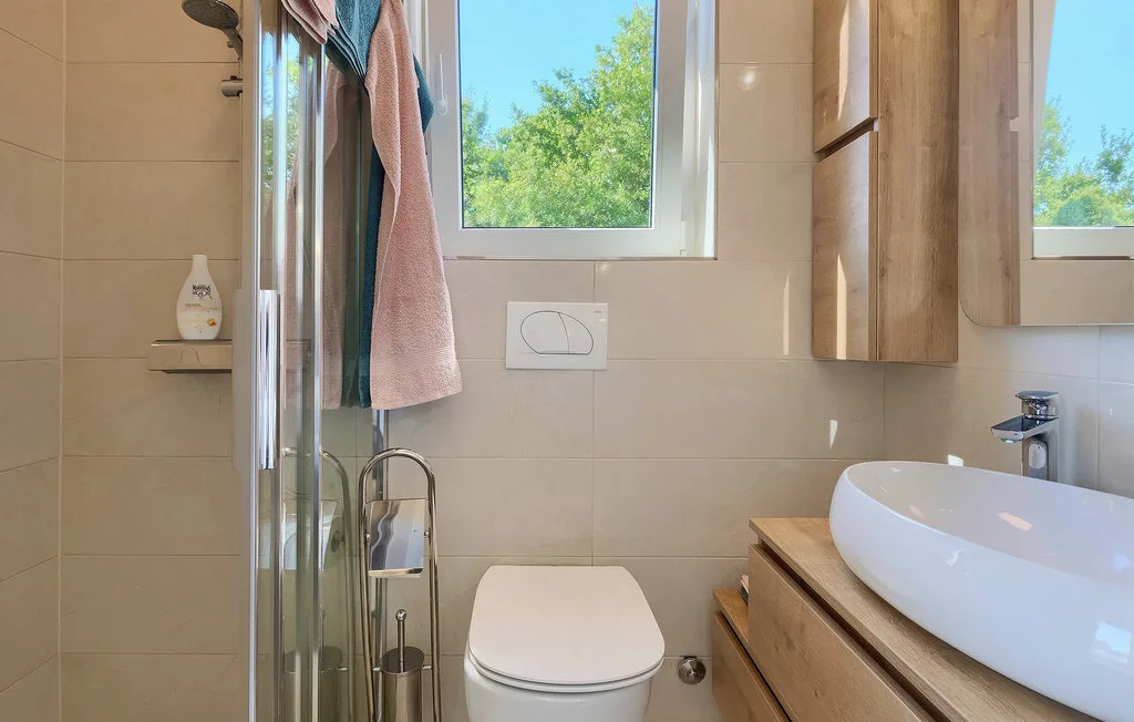 Un baño luminoso con ducha, inodoro y lavabo bajo una ventana.