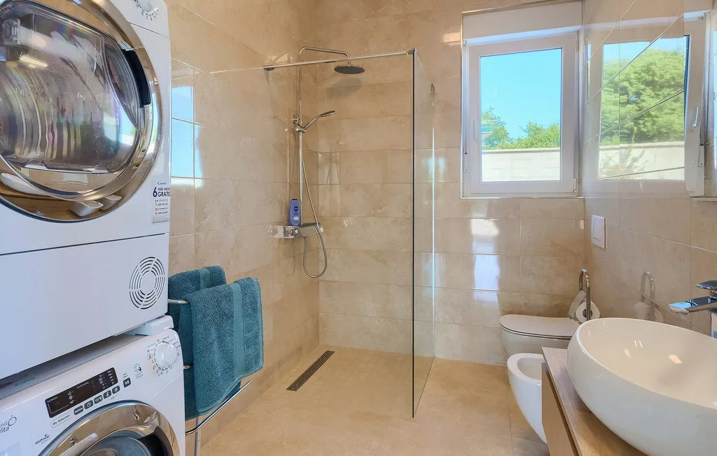 Un baño luminoso con ducha, electrodomésticos de lavandería y una ventana.