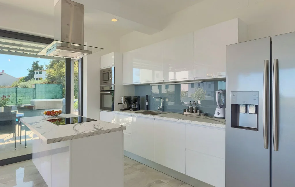Una cocina moderna y luminosa con una isla central y grandes ventanas que dan a un patio.