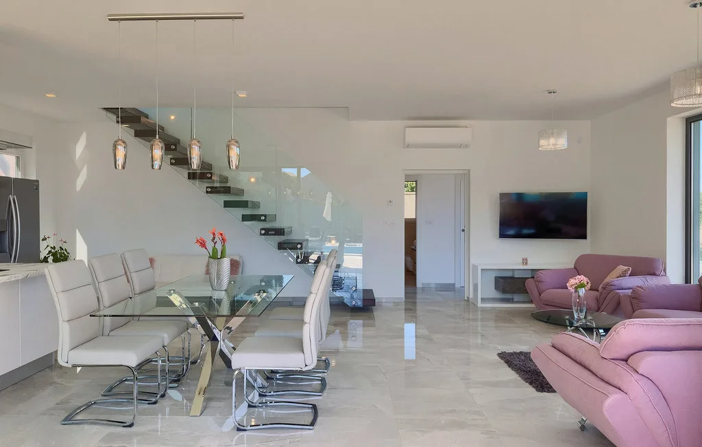 Una luminosa sala-comedor diáfana con muebles de comedor de vidrio y asientos rosados.