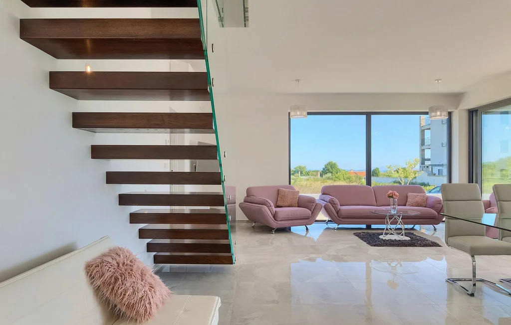 Una sala luminosa con asientos rosados junto a una escalera con barandilla de vidrio.