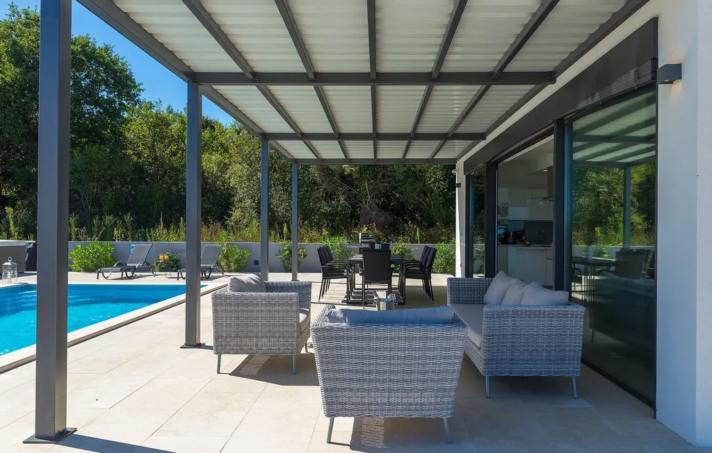 Un patio exterior cubierto con asientos junto a una piscina.
