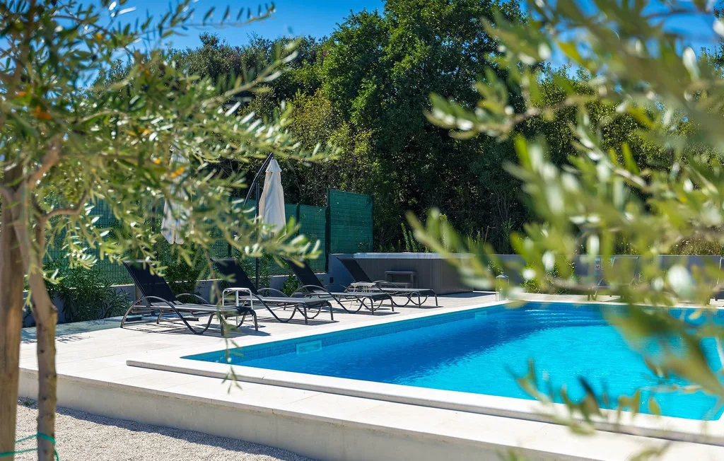 Una piscina al aire libre está rodeada de asientos reclinables y árboles frondosos.