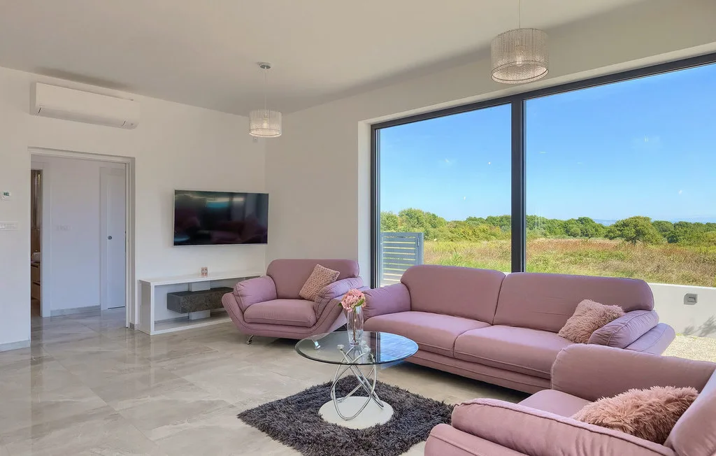 Una sala luminosa con asientos rosados y grandes ventanales con vistas a la vegetación.
