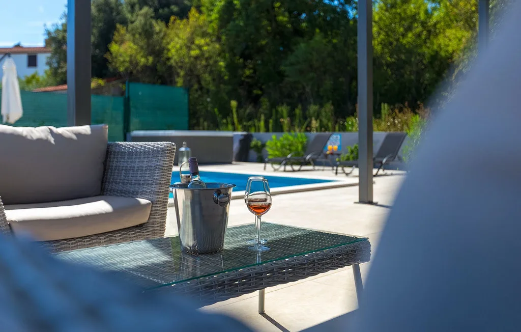 Una zona de estar al aire libre da a una piscina y a la vegetación circundante.