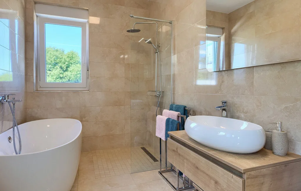 Un baño luminoso con ducha de vidrio, bañera y lavabo sobre encimera.