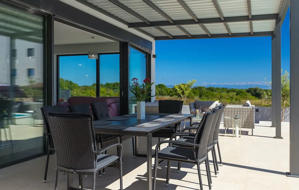 Un comedor exterior cubierto con mesa y asientos tiene vistas a la vegetación.