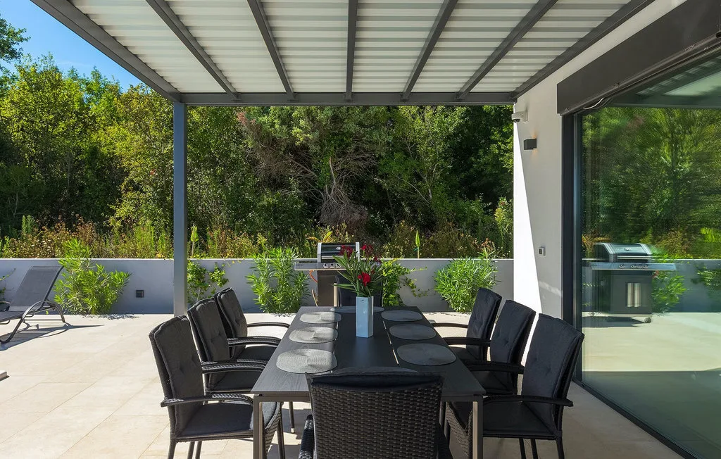 Comedor exterior cubierto con una mesa y asientos junto a puertas de vidrio.