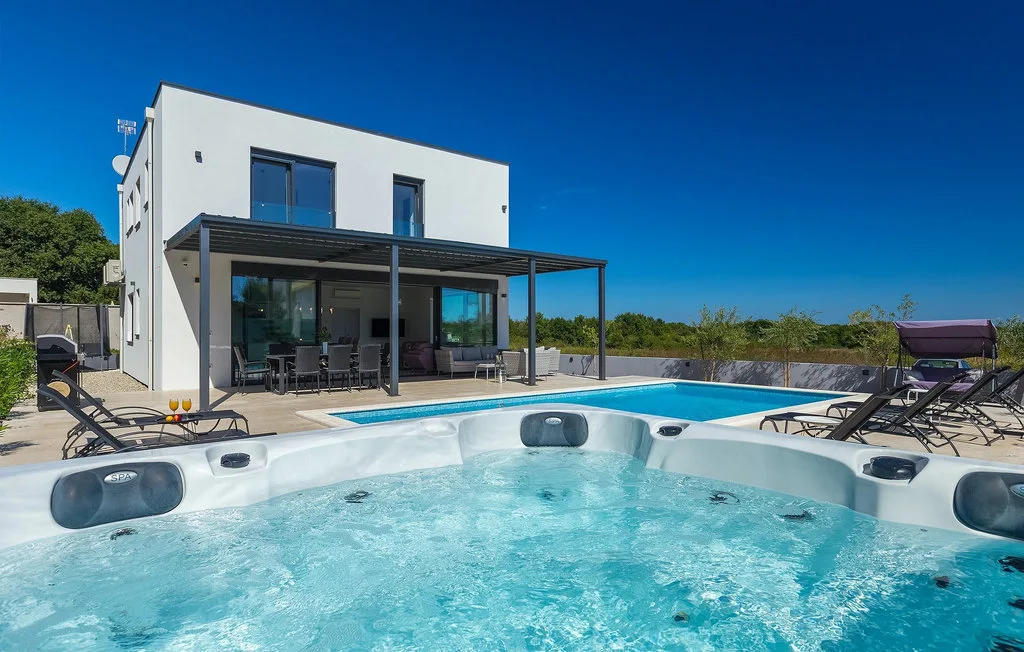 Piscina y spa al aire libre junto a una casa blanca moderna con patio sombreado.