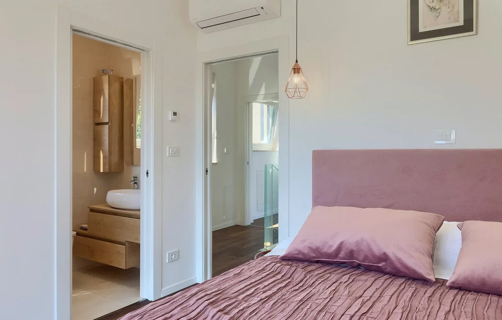 Un dormitorio con una cama malva y una puerta abierta hacia un baño.