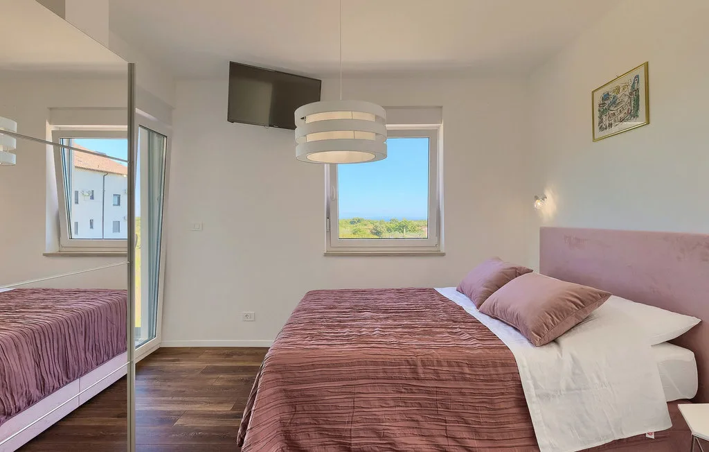 Dormitorio con una cama, armario con espejo y ventanas con vistas a la vegetación.