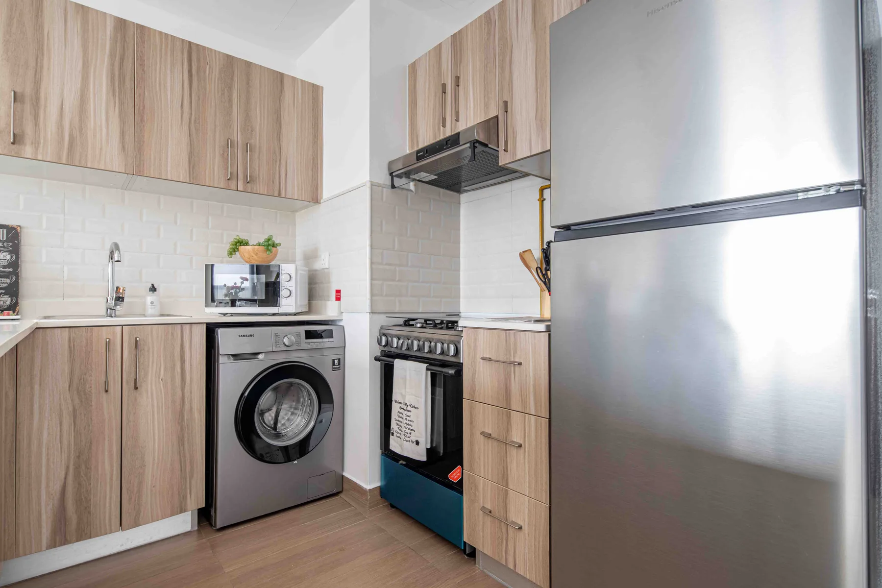Una cocina compacta con armarios de madera, una lavadora y un refrigerador grande.