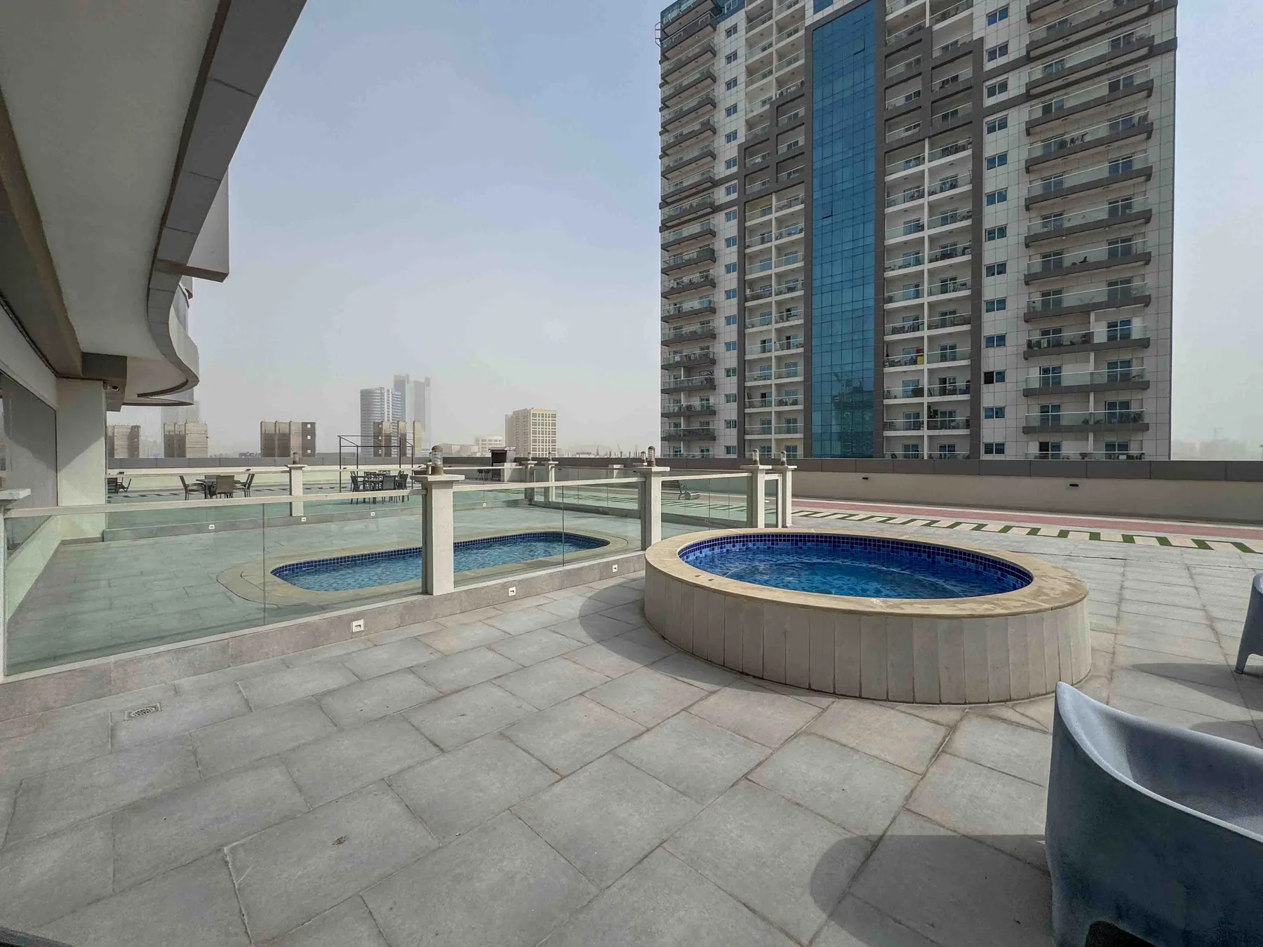 Una zona de piscina al aire libre con una piscina circular junto a un edificio alto.