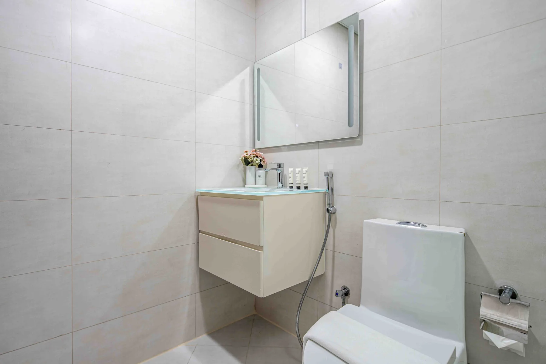 Un baño alicatado con lavabo suspendido, espejo e inodoro.