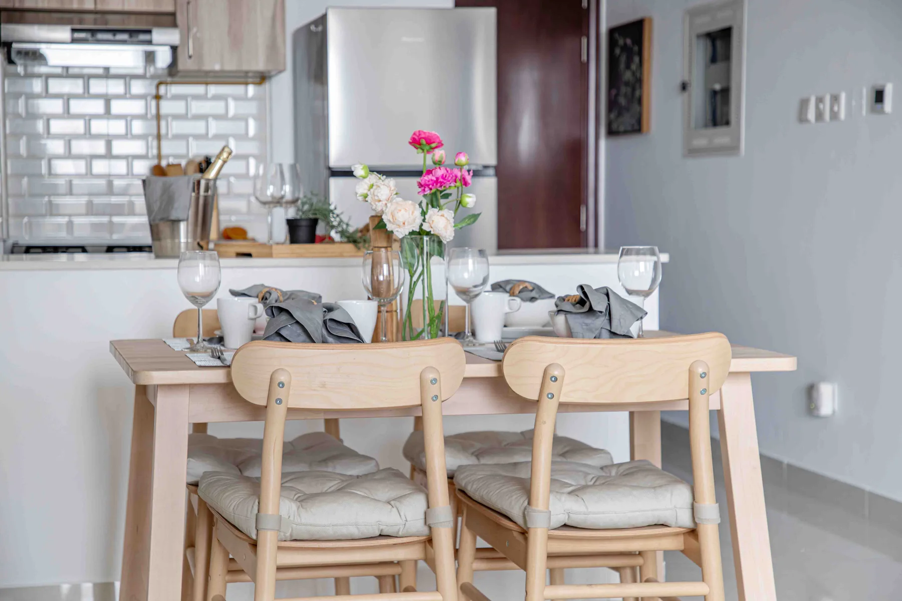 Una mesa de comedor con cubiertos y flores está junto a una cocina abierta.
