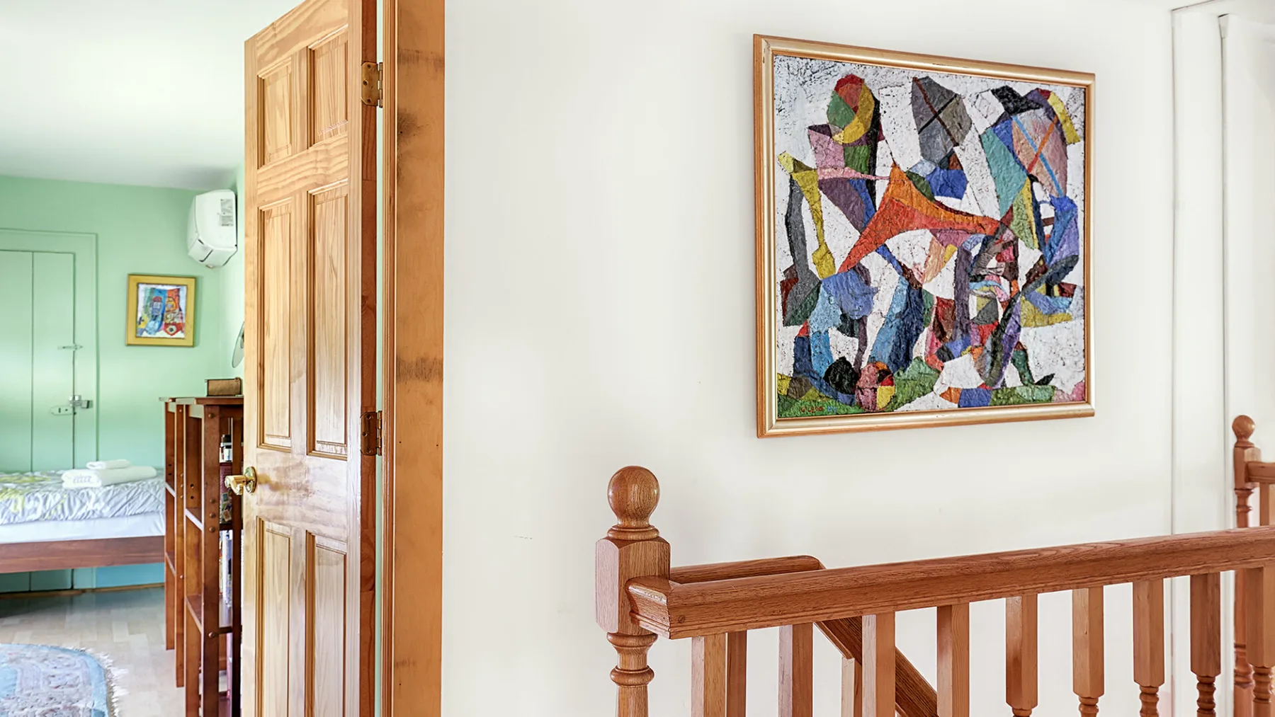 A wooden staircase railing stands beside a framed abstract painting.