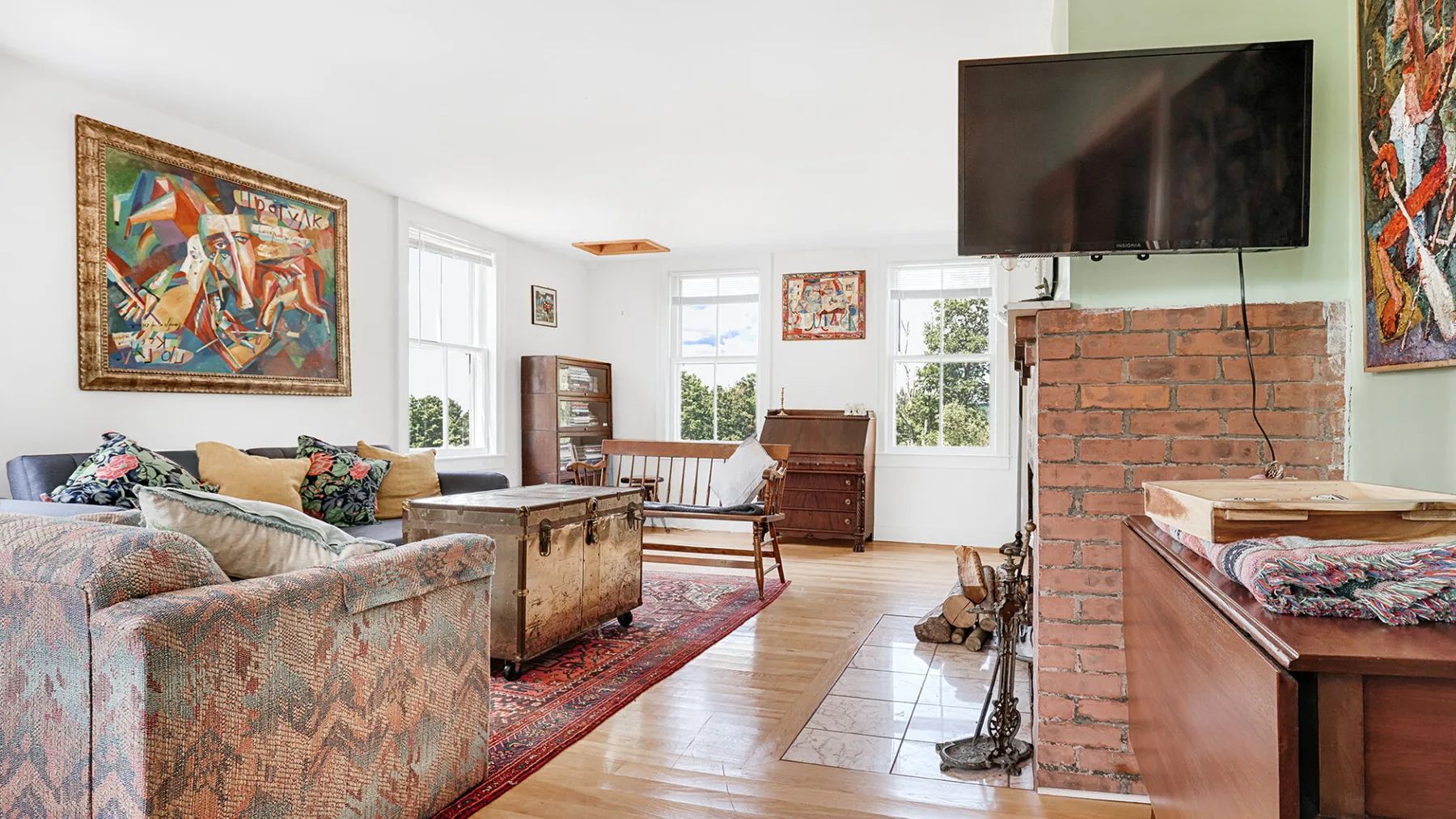A bright living room with seating, colorful artwork, and a television above the brick fireplace.
