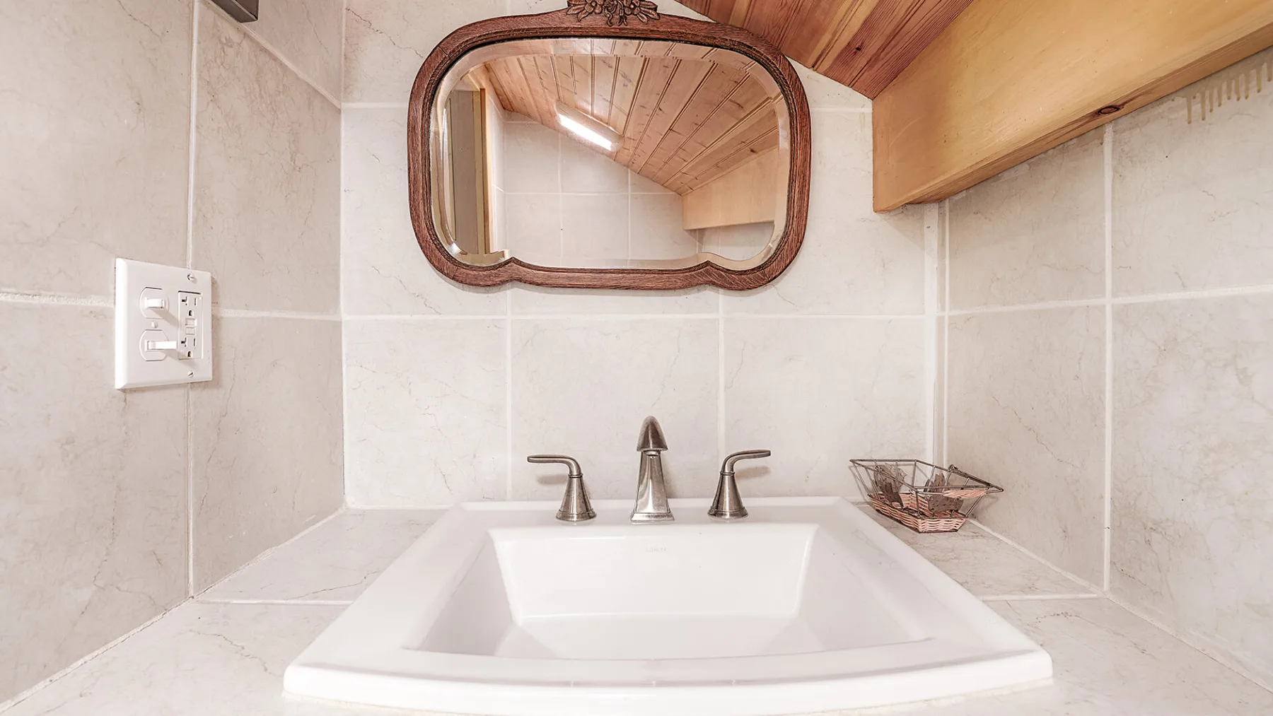 A tiled bathroom vanity with a basin, faucet, and mirror beneath a wooden ceiling.