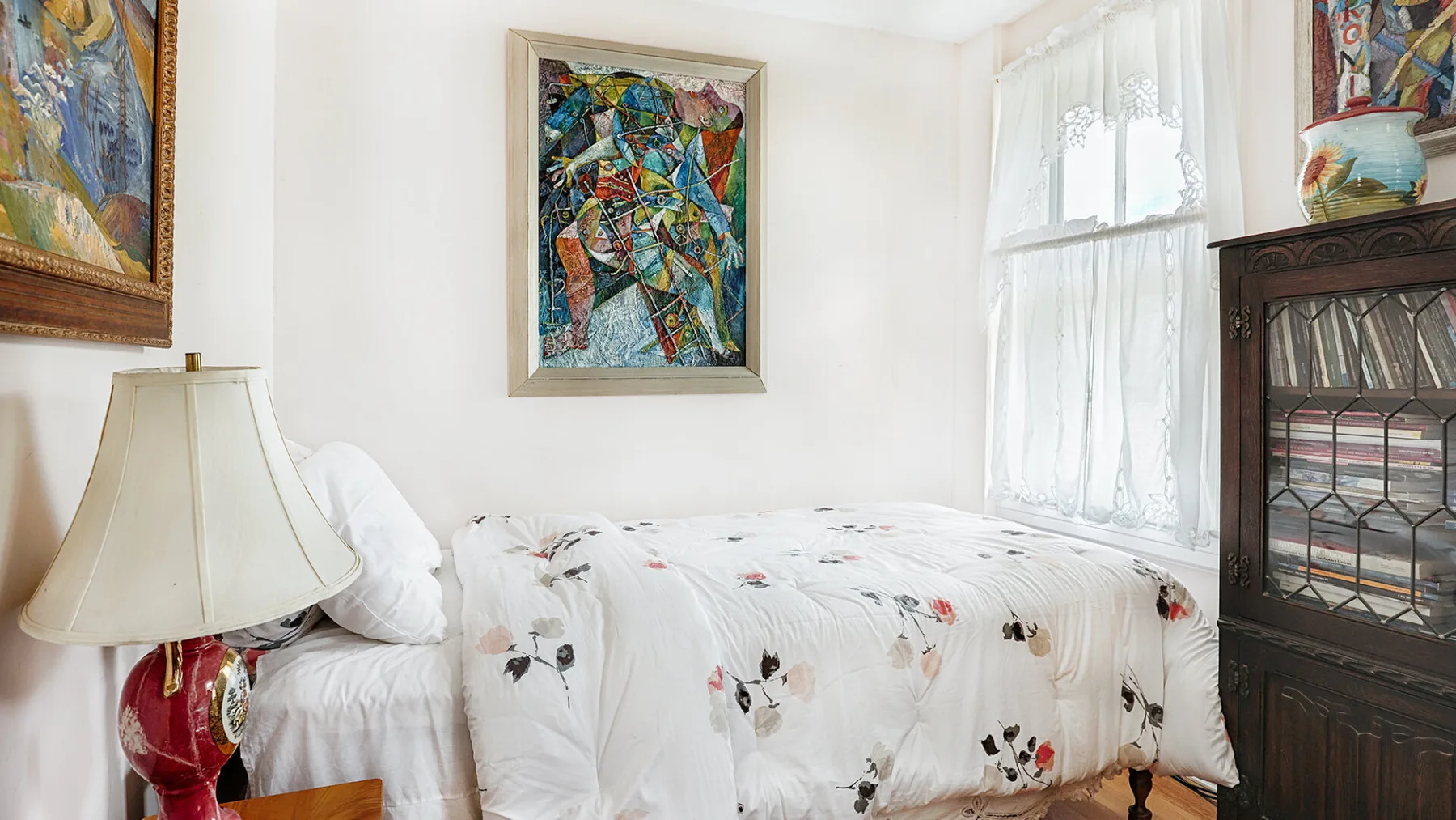 A bedroom with a floral-covered bed beside a bright curtained window.
