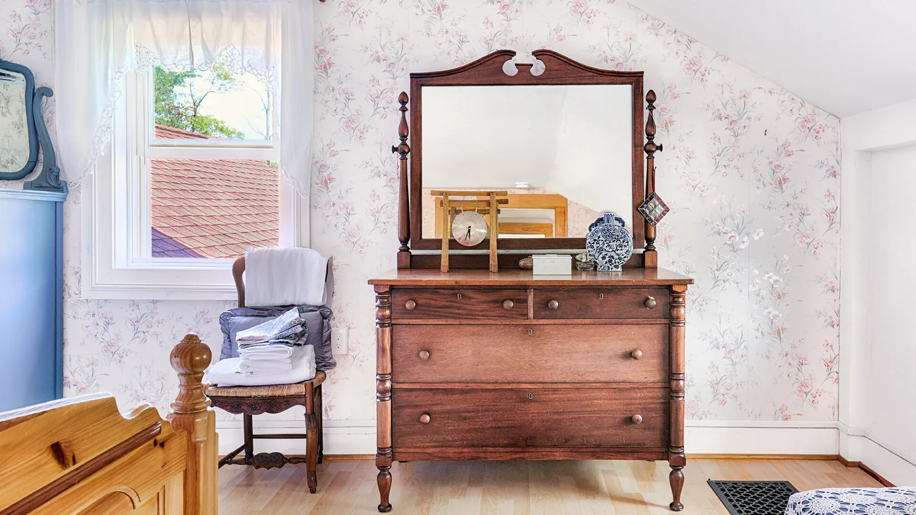 A bedroom with a wooden dresser and mirror beside a window.