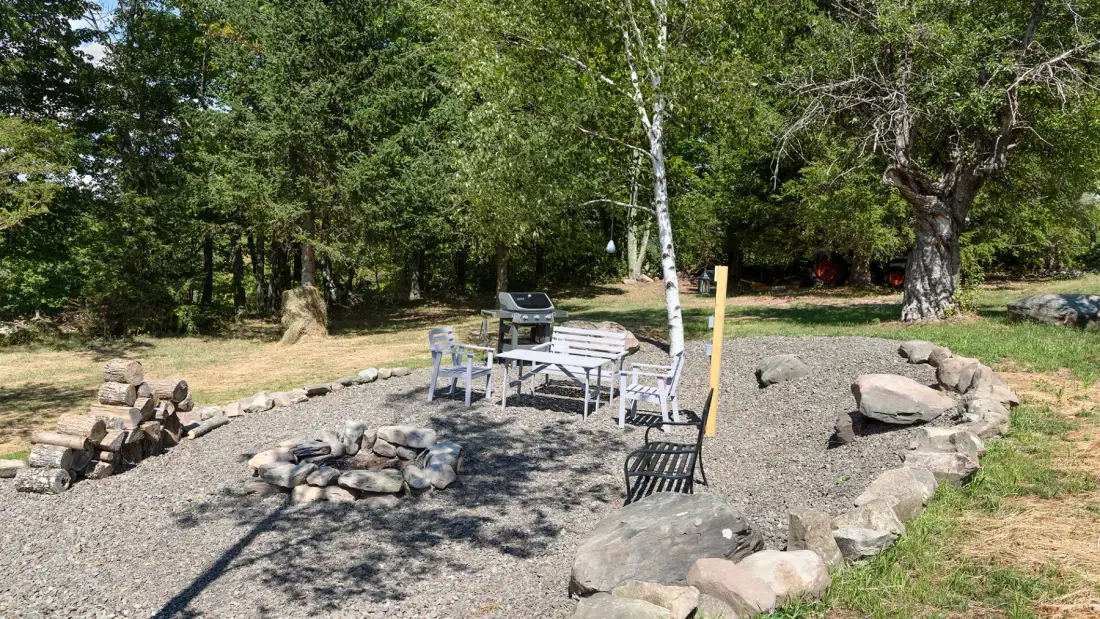 An outdoor seating area beside a stone fire pit, surrounded by trees.