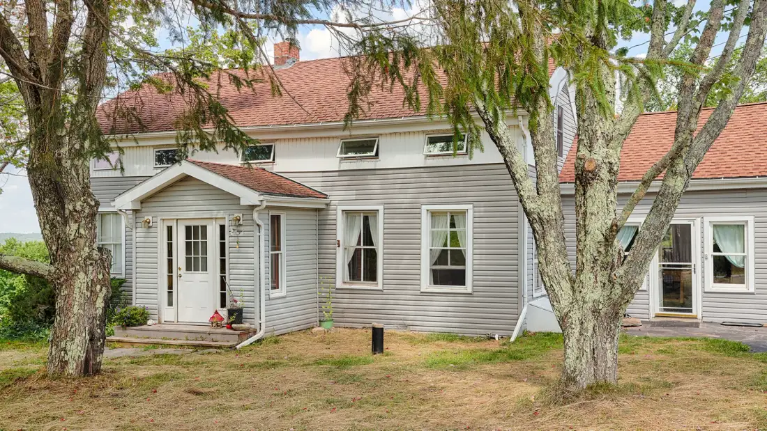 A gray-sided house with white trim stands among trees.
